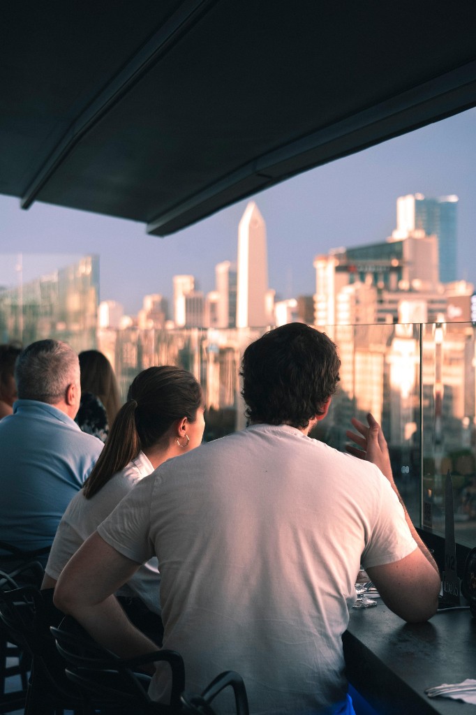 Friends talking at a rooftop bar overlooking a city skyline at sunset